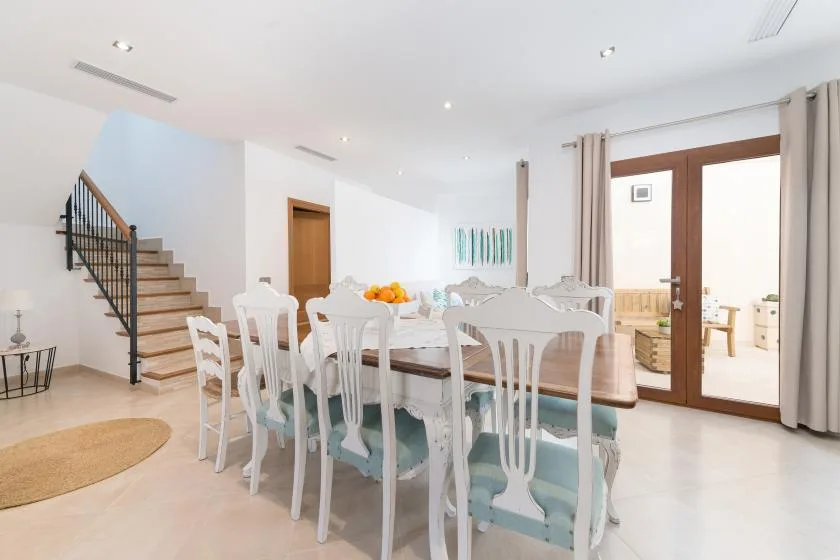 A bright dining area with a long table and white chairs beside glass doors.