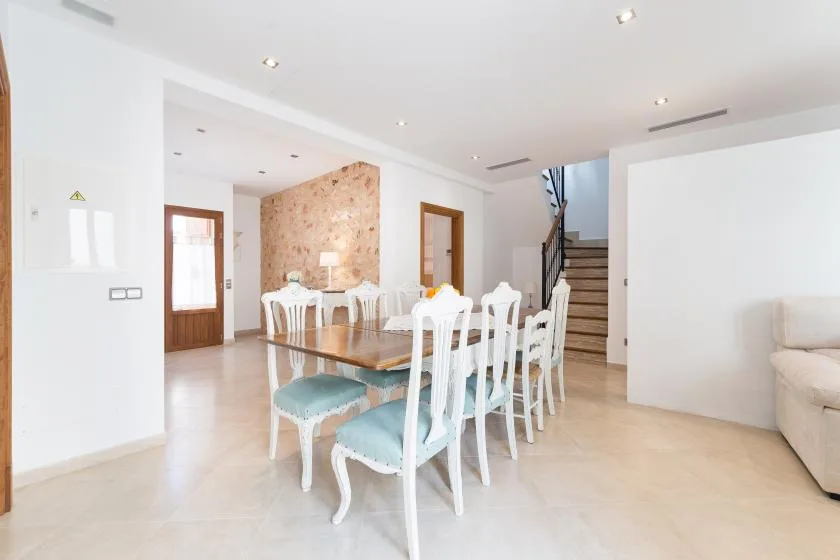 A bright dining area has a long table with white chairs beside a staircase.