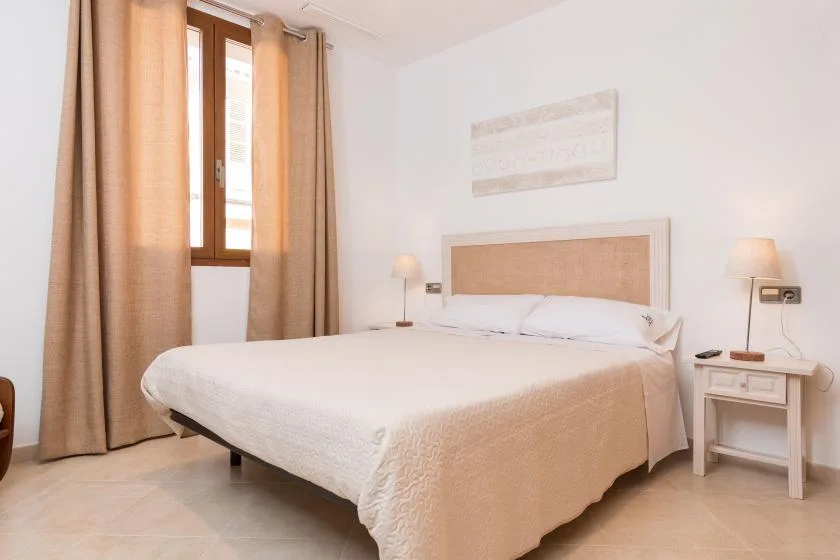 A bright bedroom with a neatly made bed and curtains beside the window.