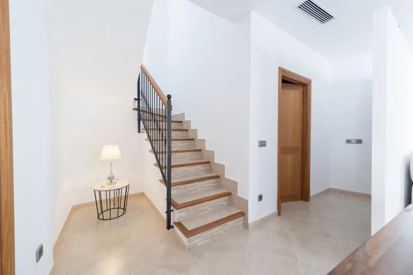 A bright interior hallway features a staircase and a wooden door.