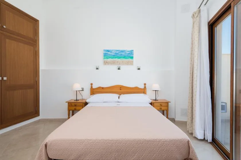 A bedroom with a double bed, matching bedside tables, and a sliding glass door.