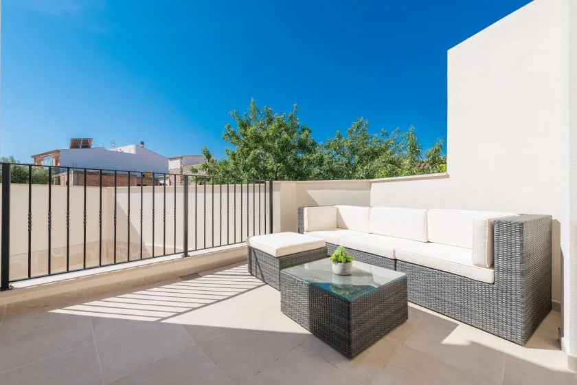 A sunny outdoor terrace has a cushioned seating area and a low table.