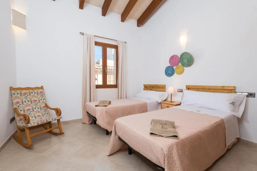 A bright bedroom with two beds, a window, and a wooden rocking chair.