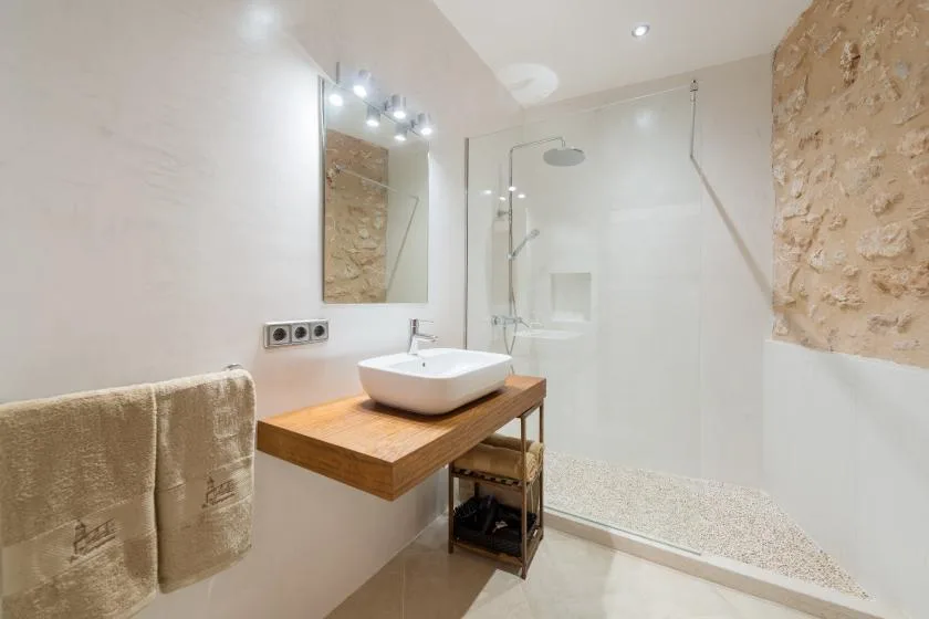 A bright bathroom with a wall-mounted sink, wooden vanity, and walk-in shower.