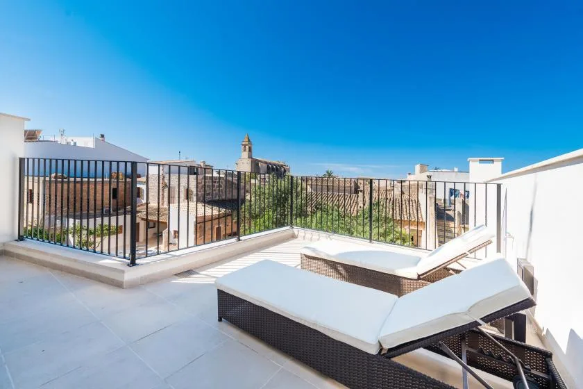 A rooftop terrace with reclining loungers and a black metal railing overlooks nearby buildings.