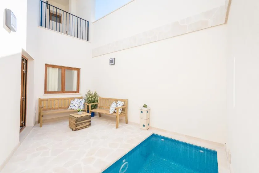 A small indoor pool sits beside wooden seating in a bright courtyard.