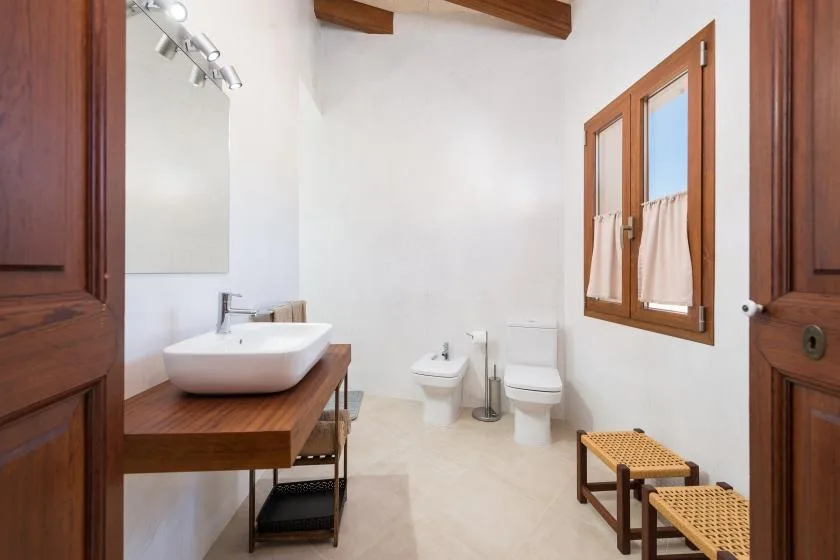 A bright bathroom with a sink, toilet, and a wood-framed window.