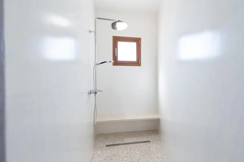 A bright shower room with a wall-mounted shower and a small window.