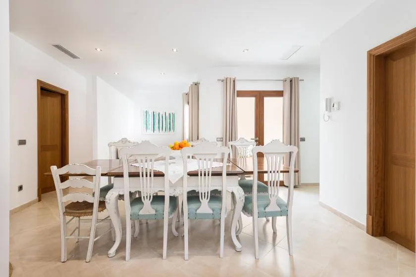 A bright dining room with a long table and white chairs.