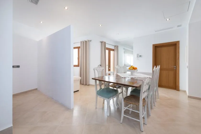 A bright dining area with a long table and chairs beside curtained windows.