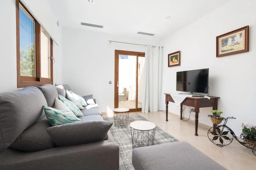 A bright living room with a gray seating area, a television, and a glass coffee table.