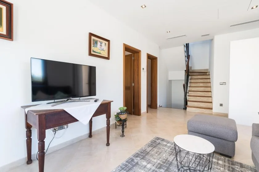 A bright living area with a television, seating, and stairs at the back.