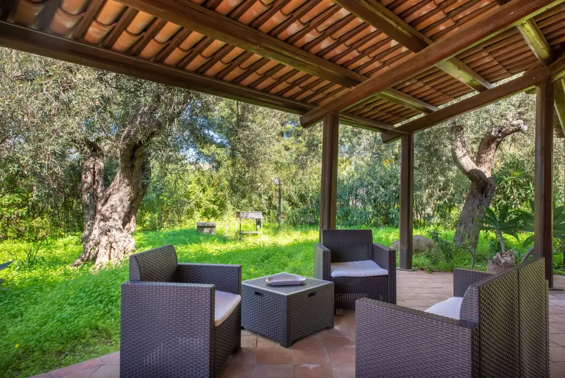 A covered outdoor seating area with a low table overlooks a green garden.