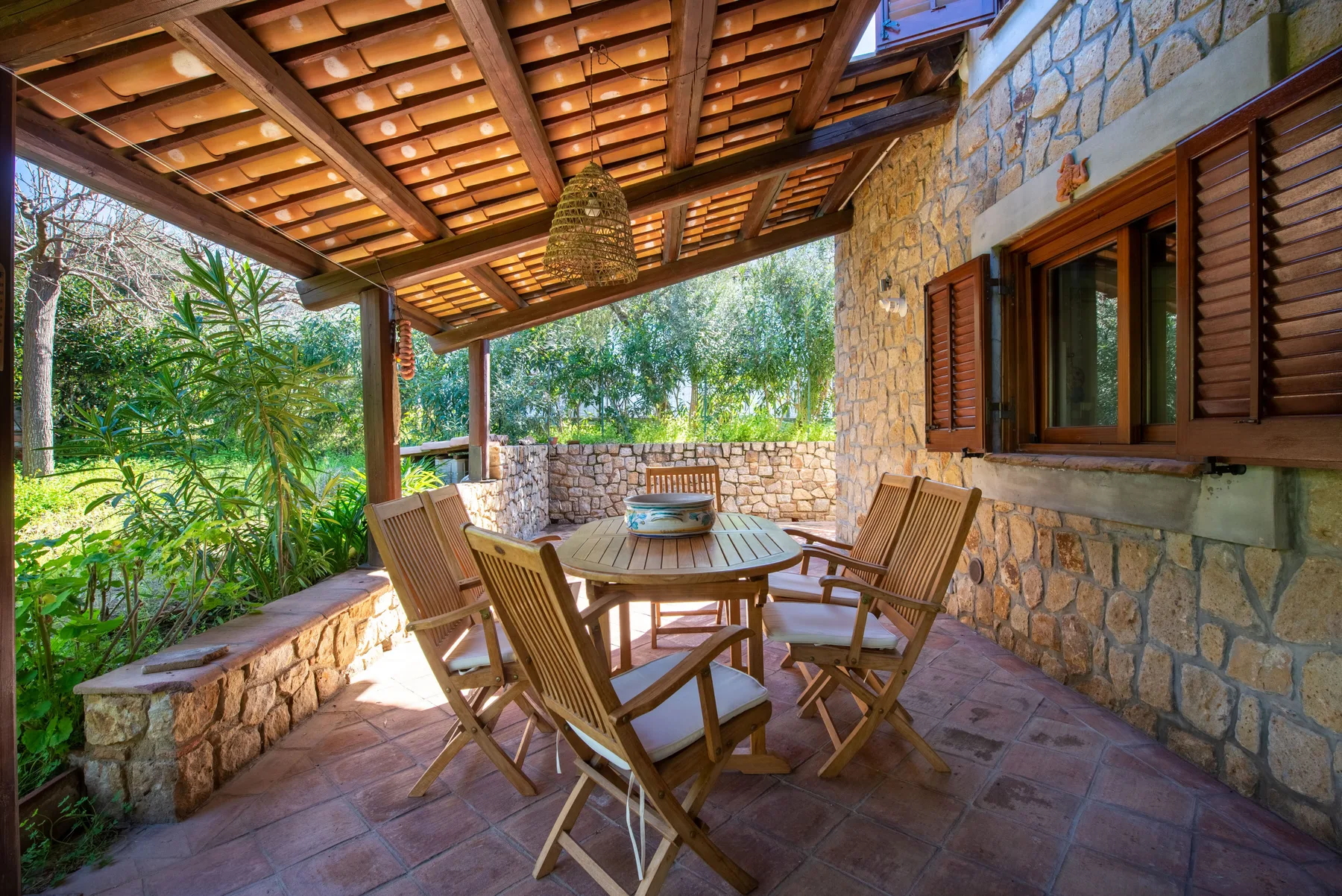 A covered stone patio with a round table and outdoor seating.