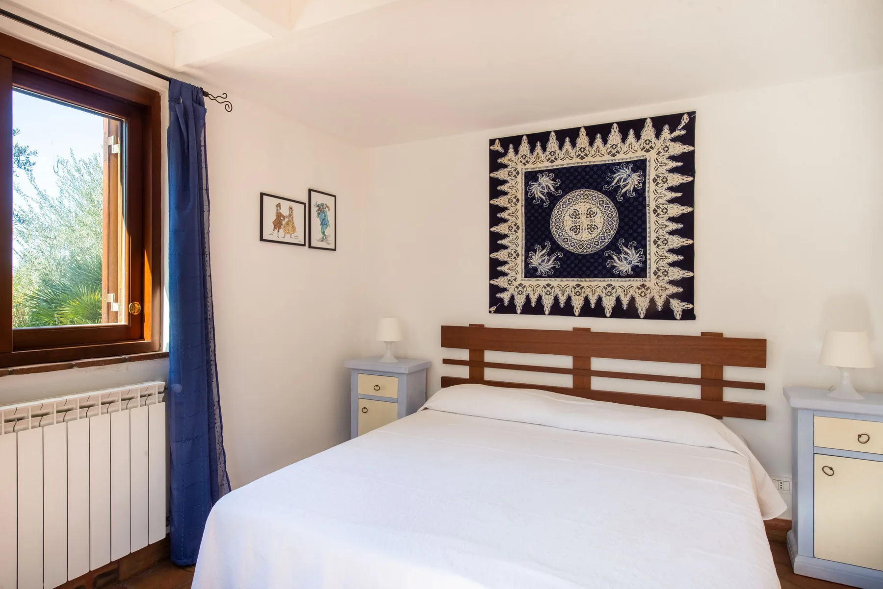 A bedroom with a neatly made bed beneath a decorative wall hanging.