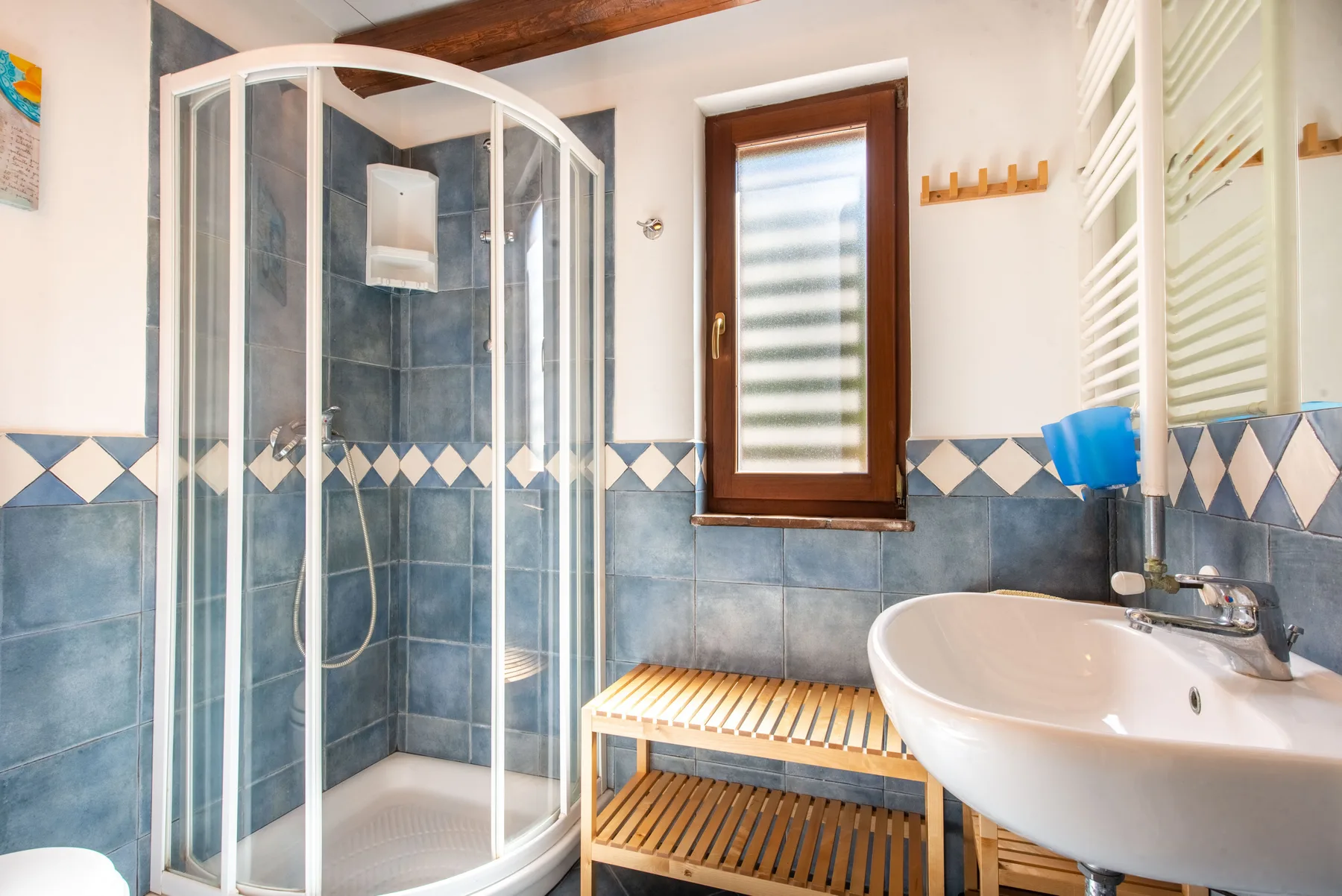 A tiled bathroom with a curved glass shower and a wall-mounted sink.
