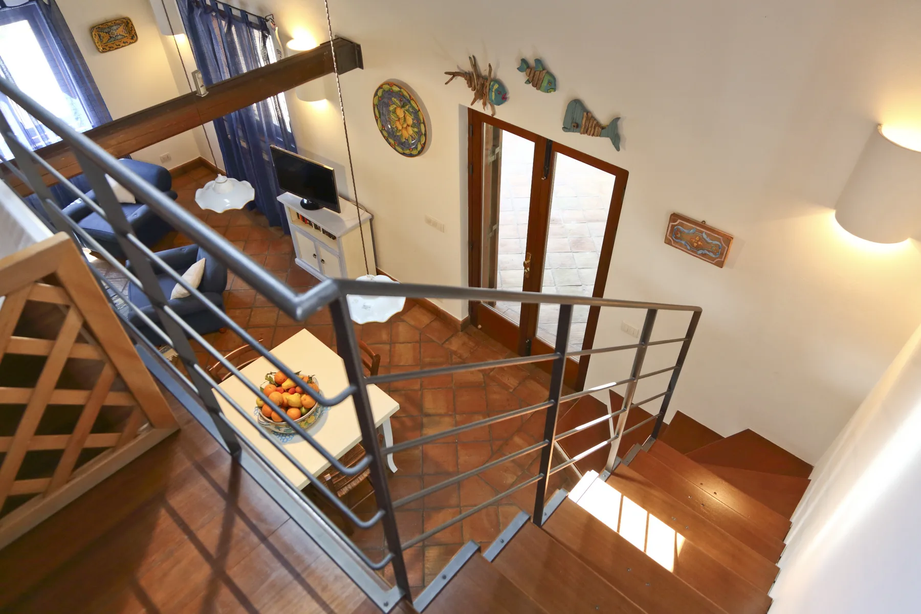 A wooden staircase with metal railings overlooks a tiled living area.