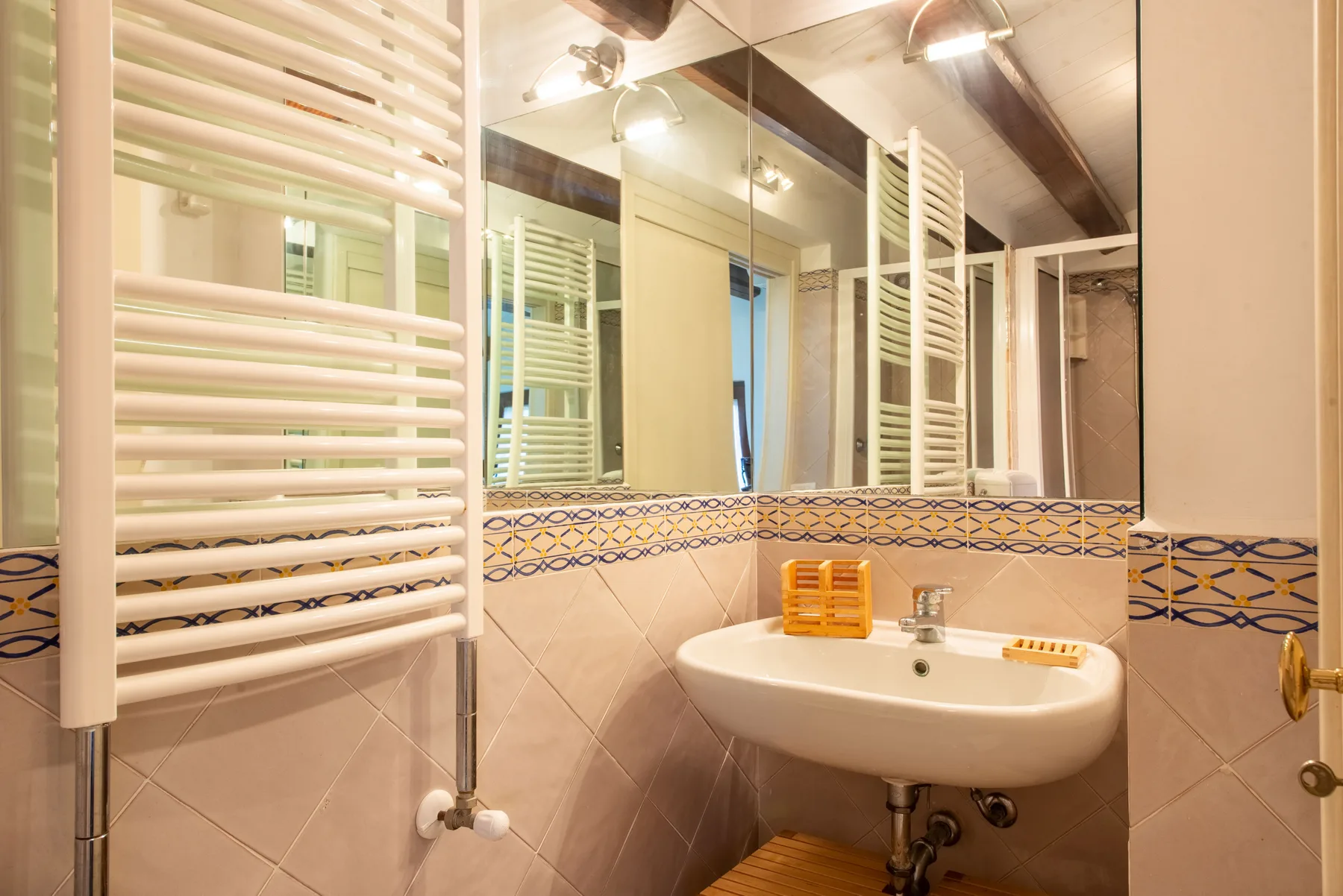 A bathroom with a sink, mirrored walls, and a wall-mounted towel warmer.
