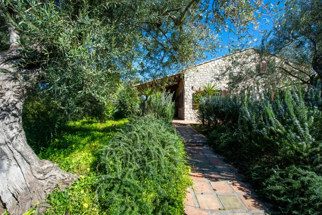 A garden path leads through greenery to a stone building.