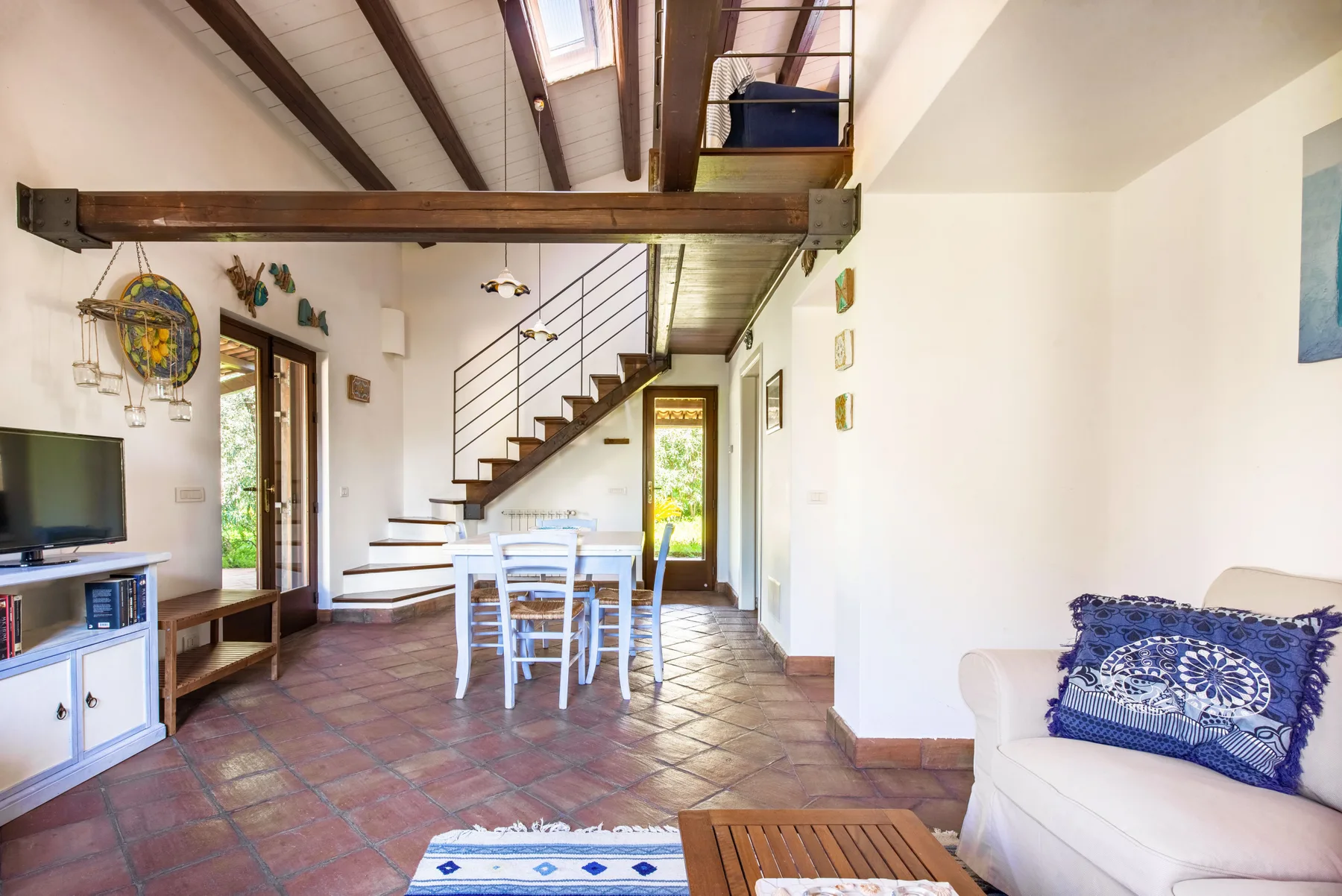 A bright living and dining area with a staircase and exposed ceiling beams.