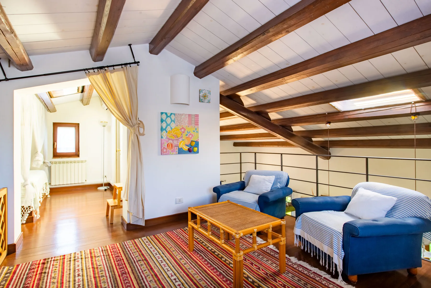 A bright living room with blue seating, a wooden coffee table, and exposed ceiling beams.