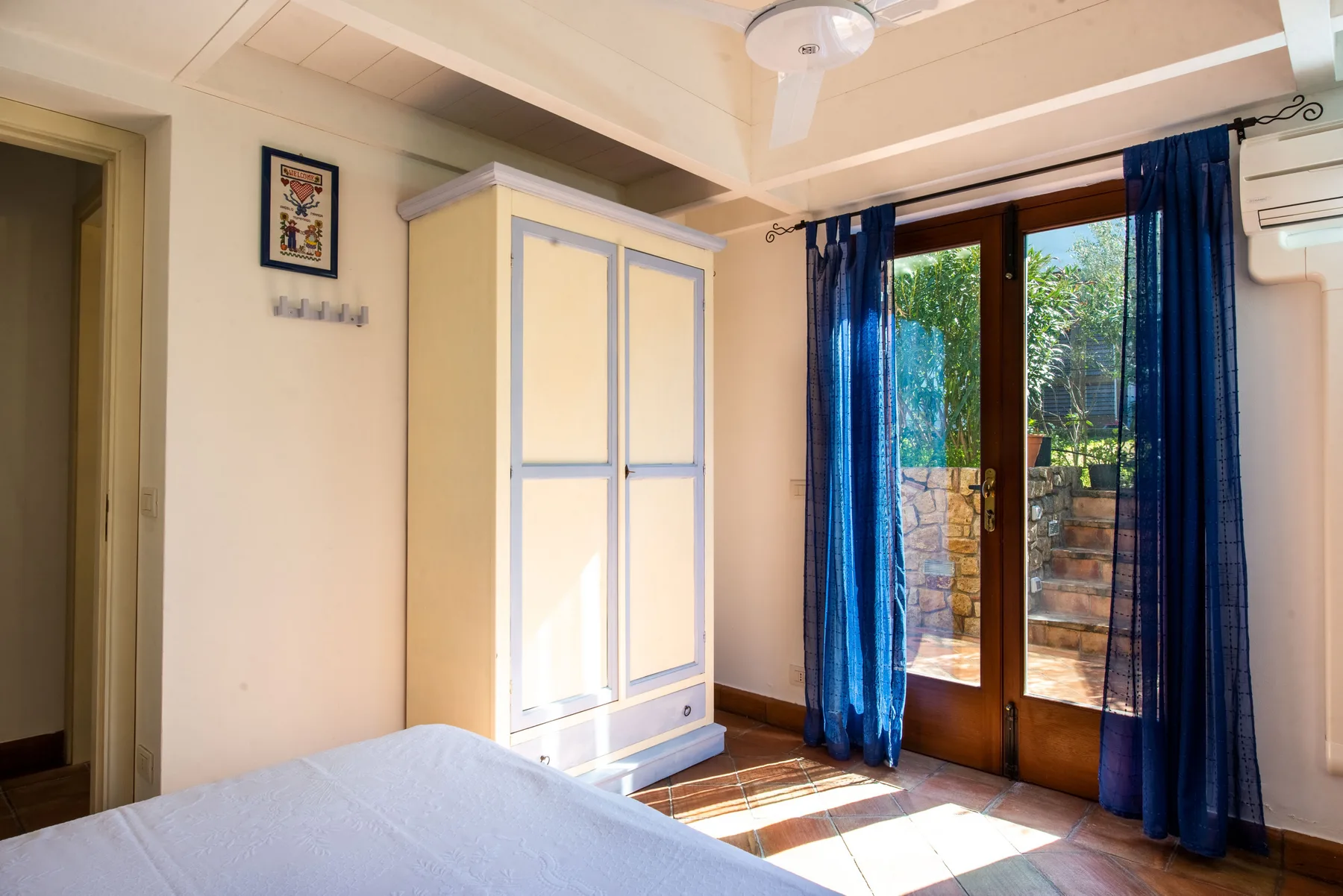 A bedroom with a bed, a wardrobe, and glass doors opening onto a patio.