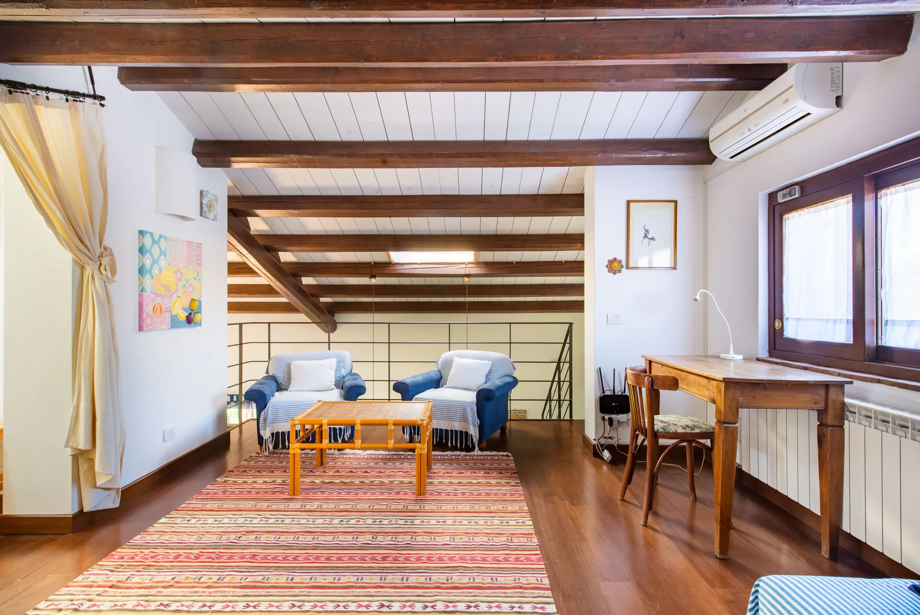 A bright living room with seating beneath exposed wooden ceiling beams.