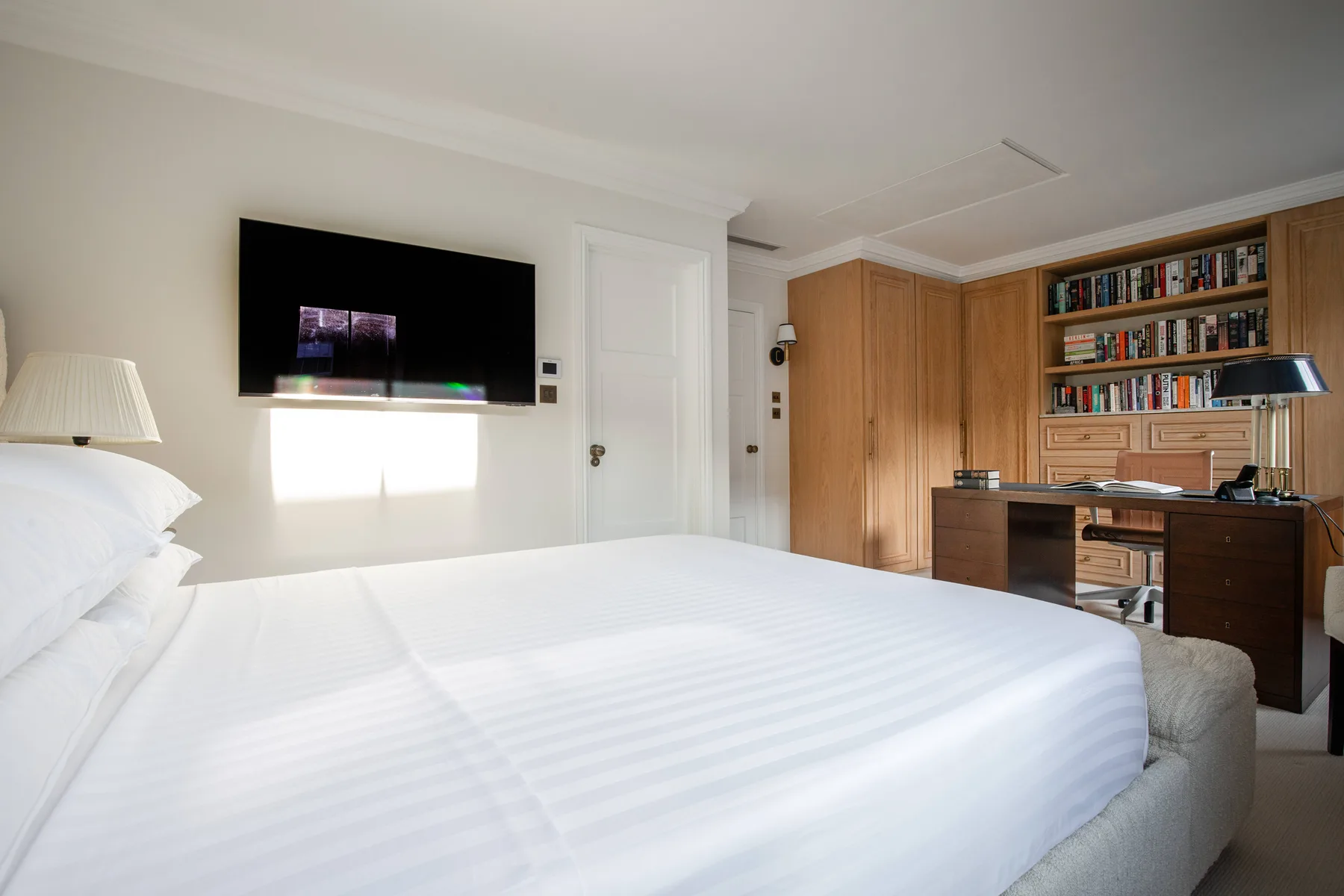 A bright bedroom with a neatly made bed and wooden built-in cabinets.