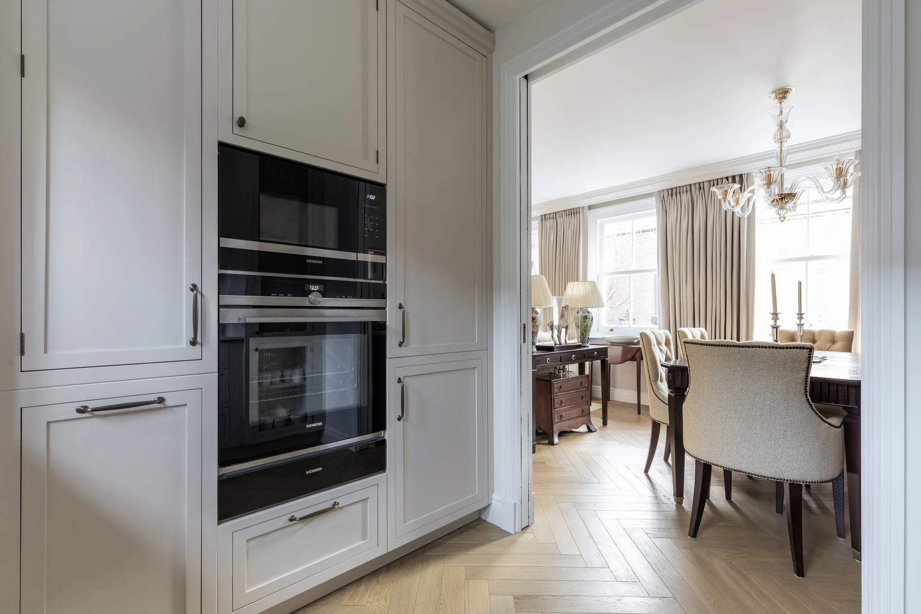 Built-in kitchen appliances open onto a bright dining area with a table and chairs.