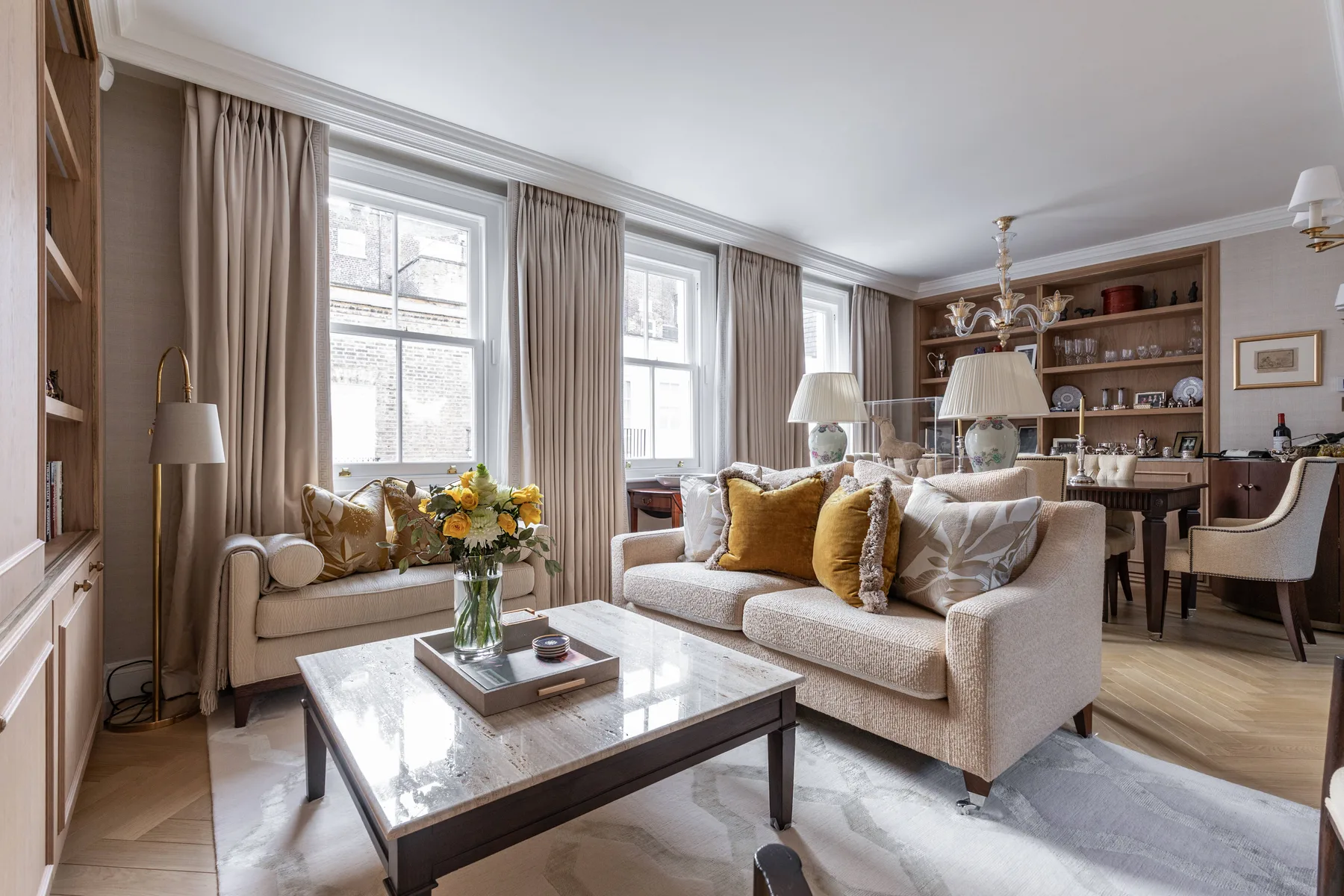 A bright living room with a seating area, coffee table, and tall curtained windows.