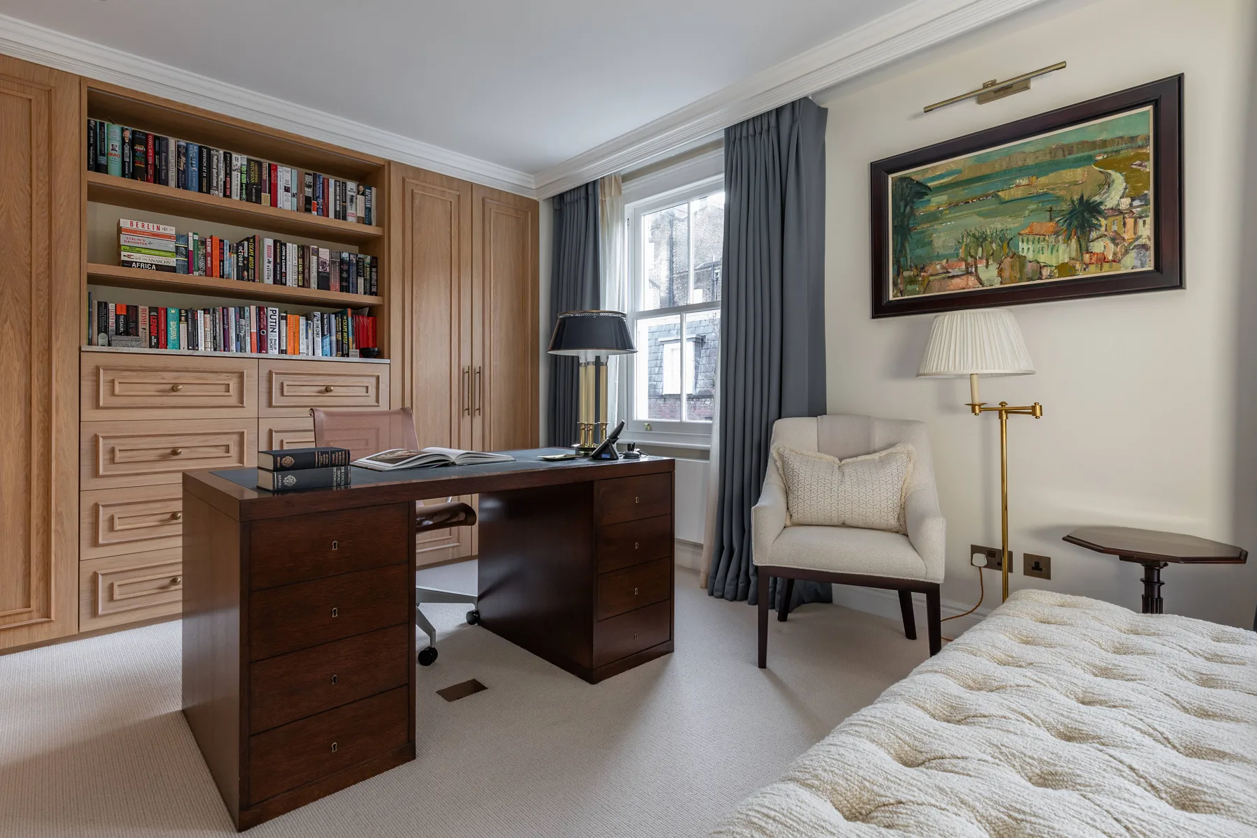 A bedroom workspace with a desk, a reading chair, and a large window.