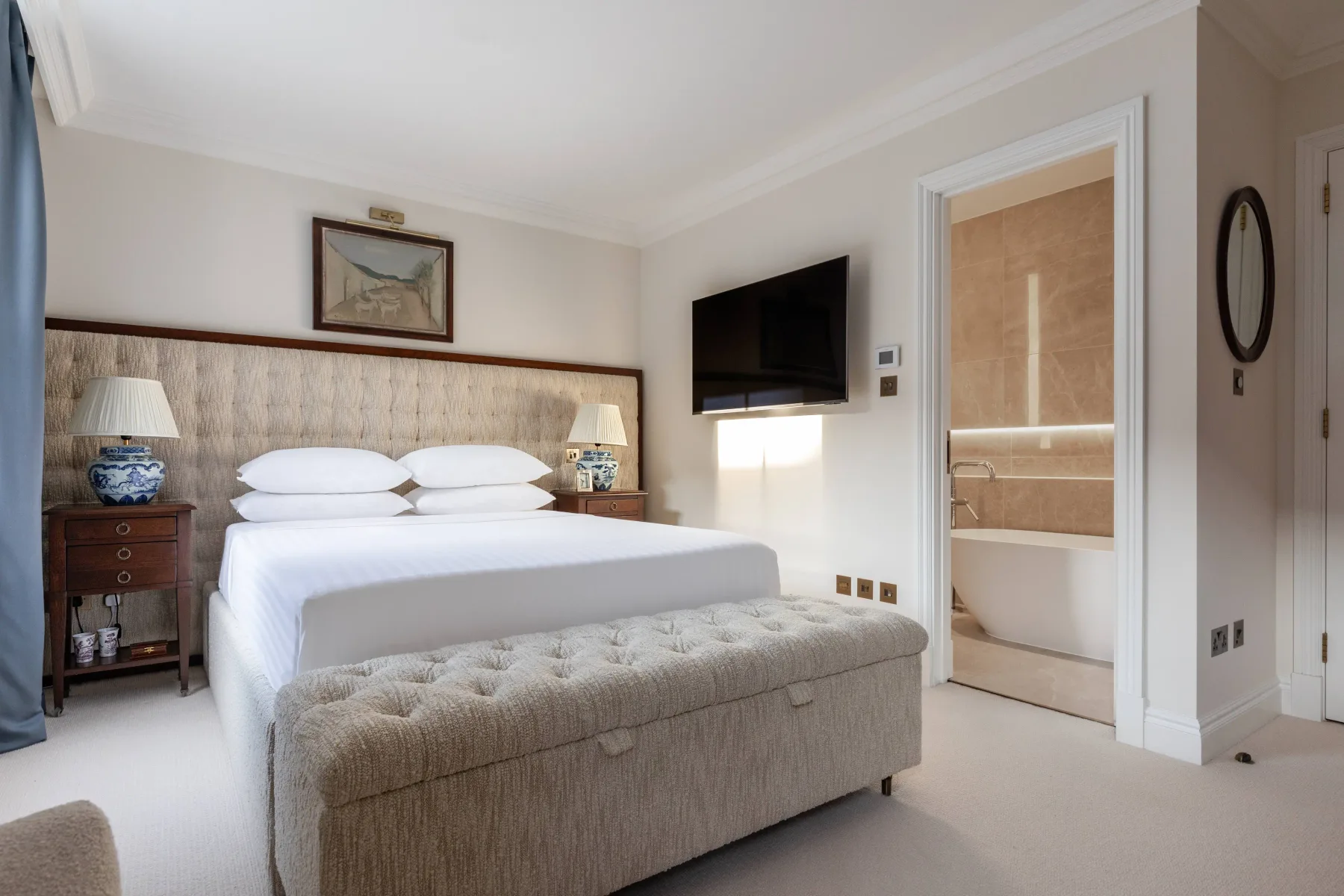 A bedroom with a large bed, upholstered bench, and wall-mounted television.