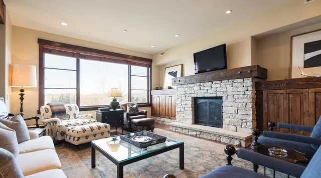 Una sala de estar con asientos, una chimenea de piedra y ventanas grandes.
