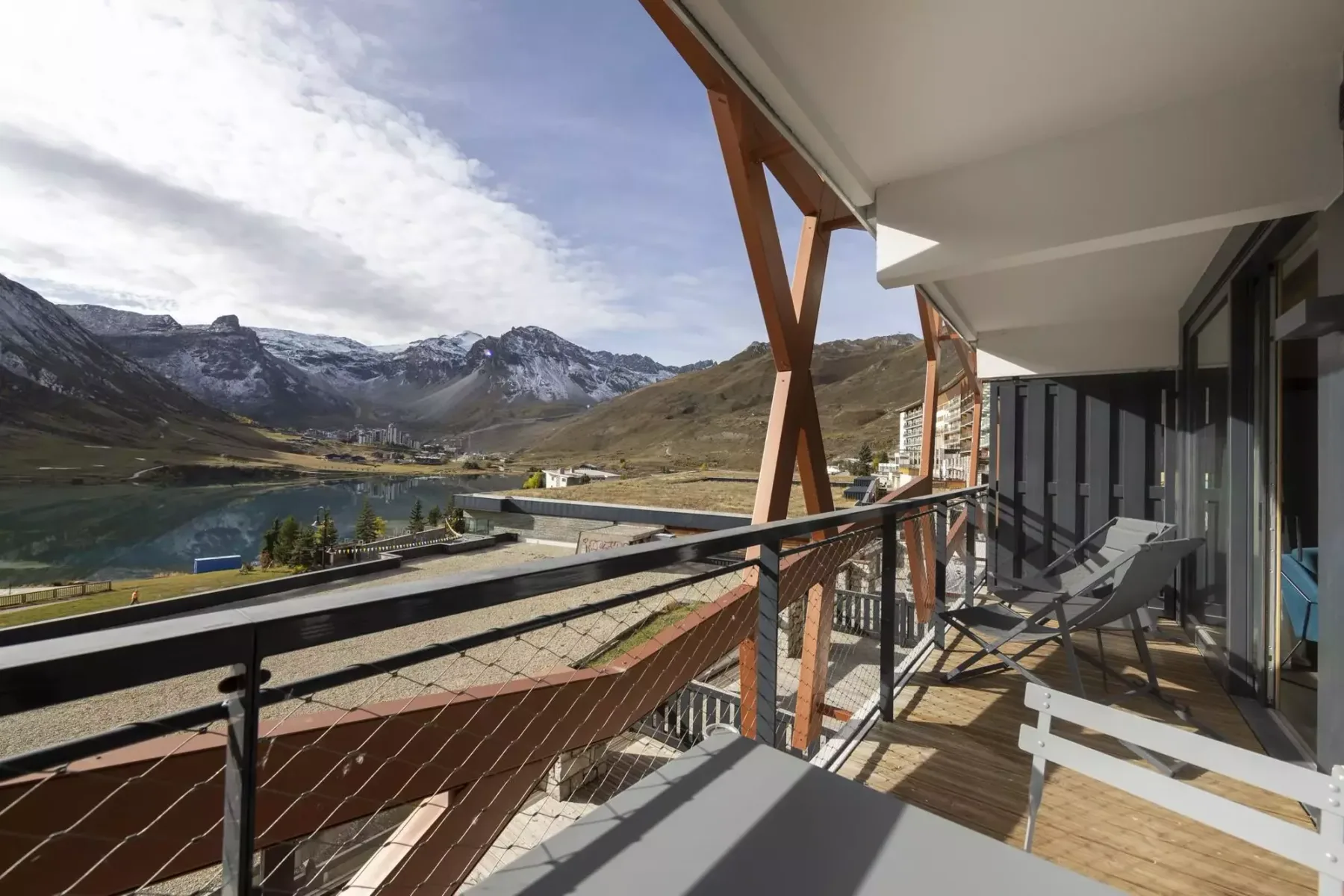 A balcony with outdoor seating overlooks a mountain valley and lake.