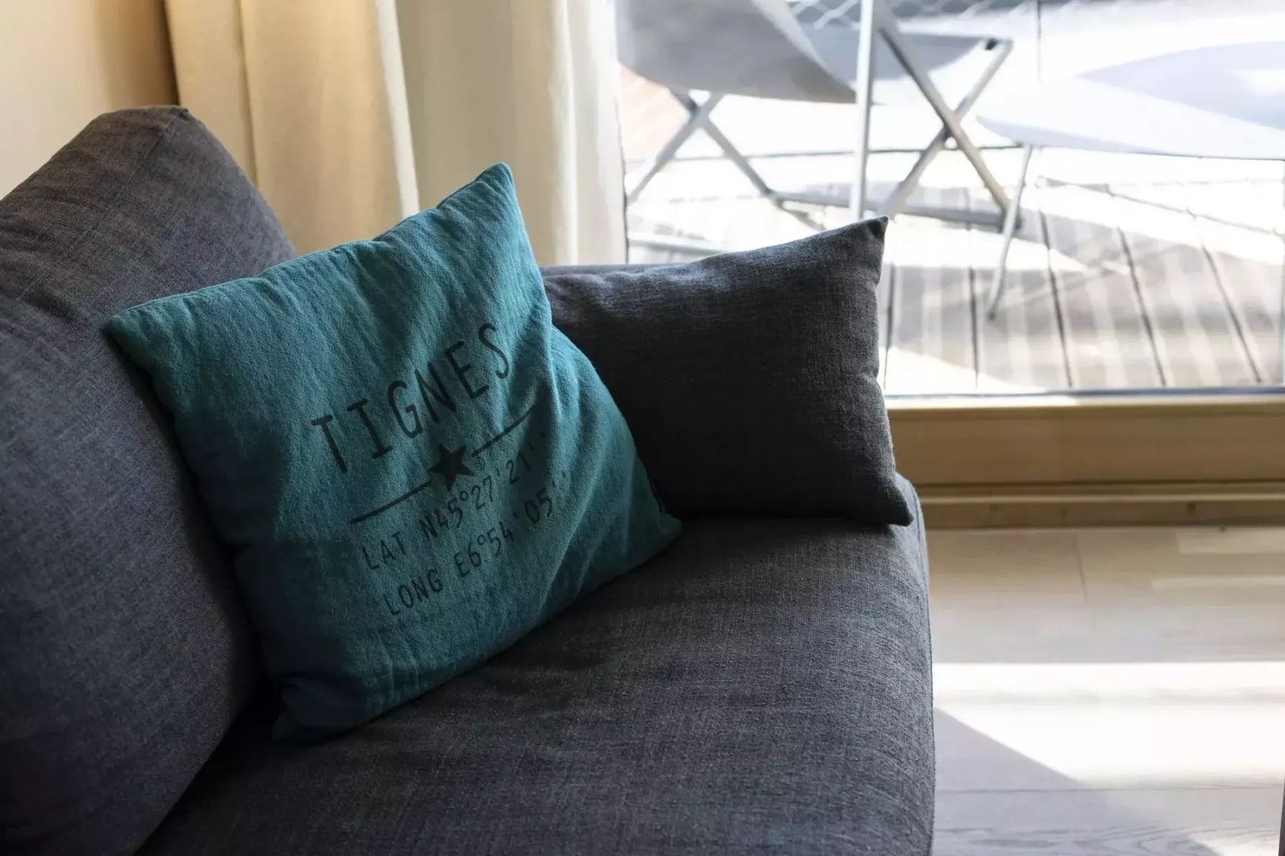 A dark upholstered seating area with a teal cushion beside a large window.