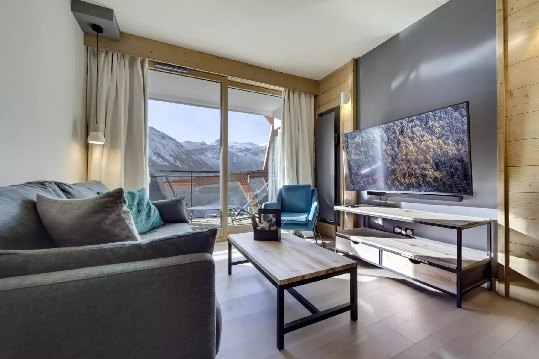 A living room with seating, a television, and a mountain view through the glass doors.
