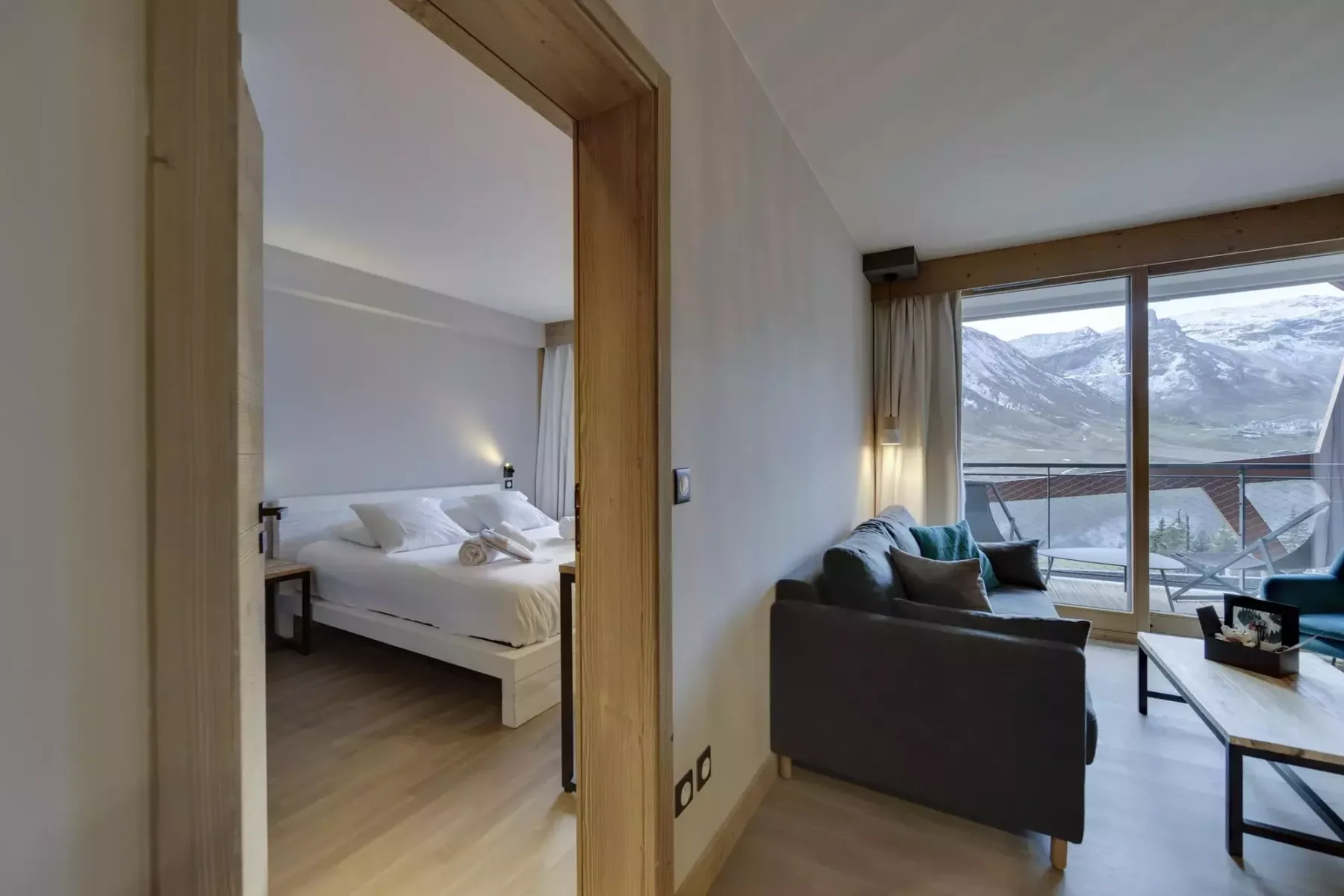 A living area opens onto a balcony with mountain views, beside a bedroom.