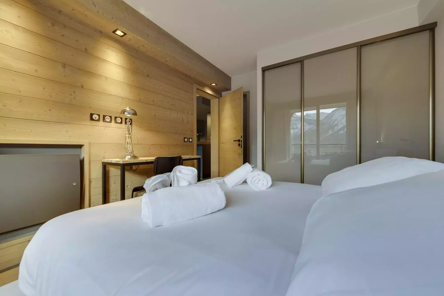 A bedroom with white bedding, rolled towels, and a wood-paneled wall.