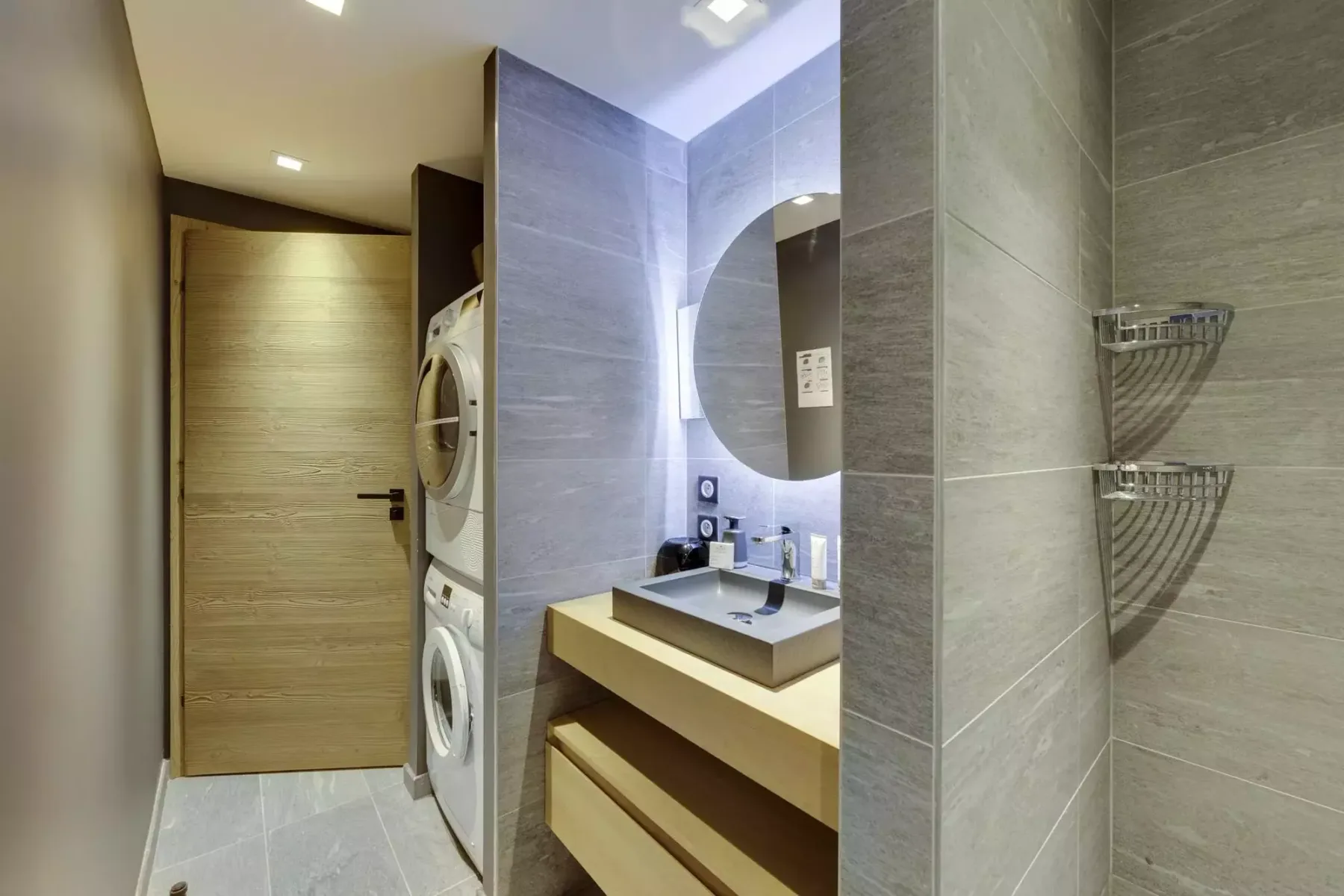 A tiled bathroom with a vanity, mirror, and stacked laundry machines.