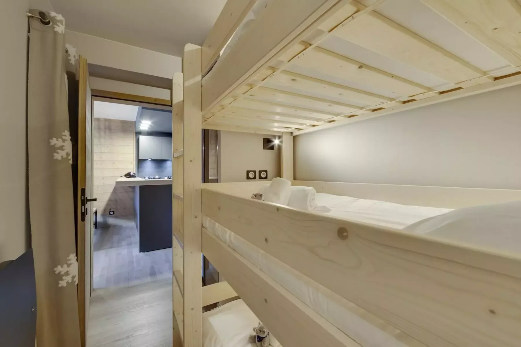 A bunk-bed sleeping area with light wood bunks and a doorway to the kitchen.