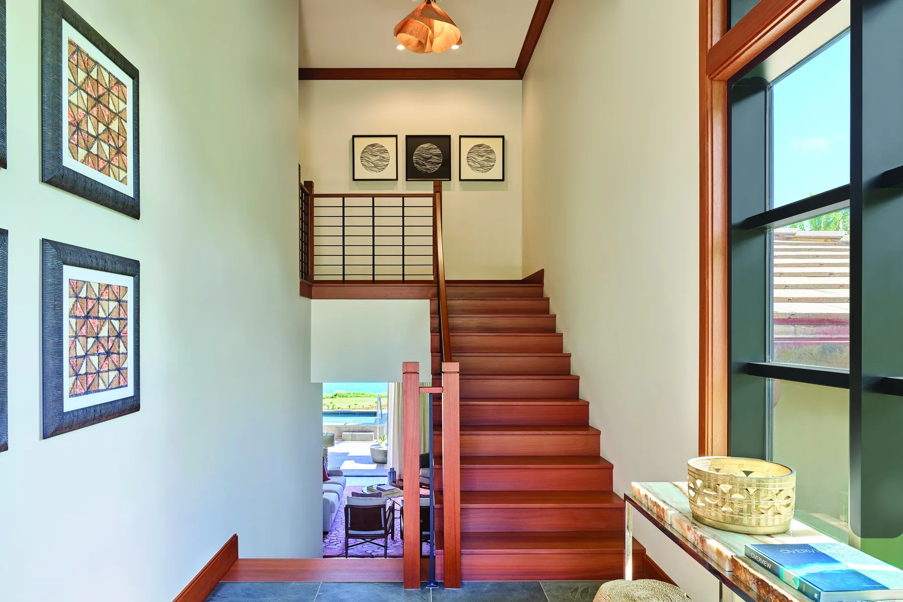 Una escalera de madera sube junto a cuadros en un interior luminoso.