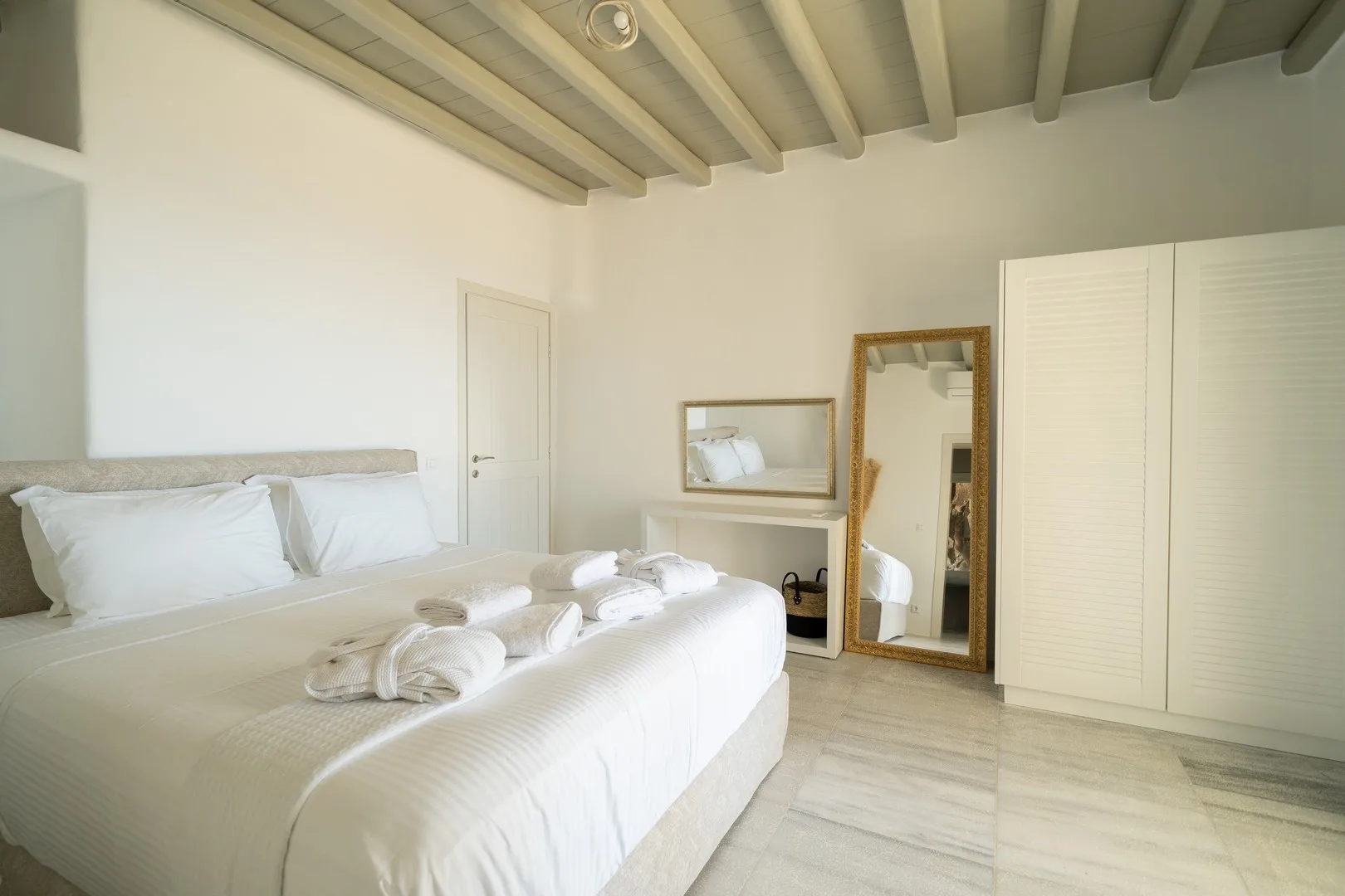 A bright bedroom with a large bed and a full-length mirror.