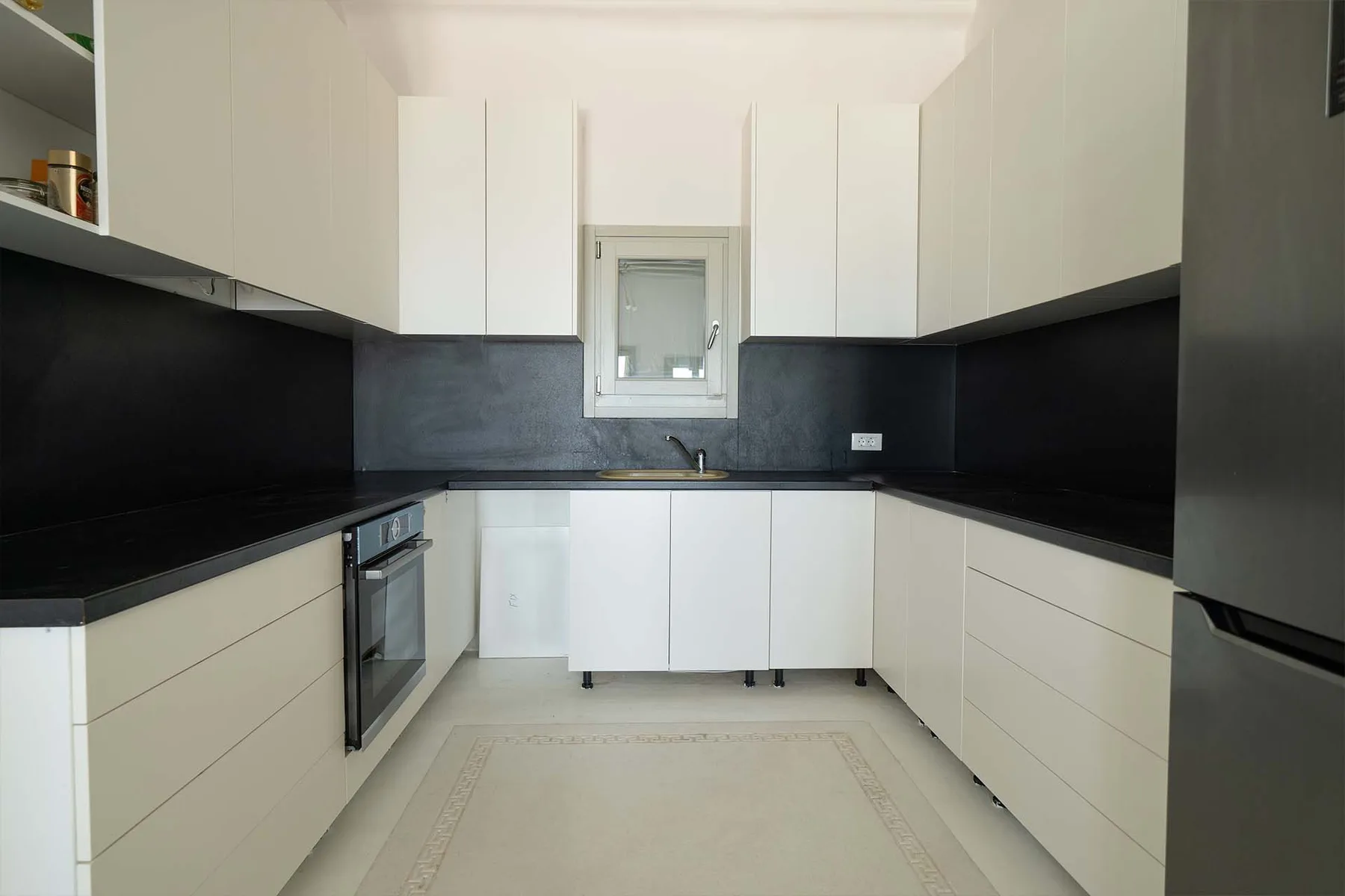 A bright modern kitchen with white cabinets and dark countertops.