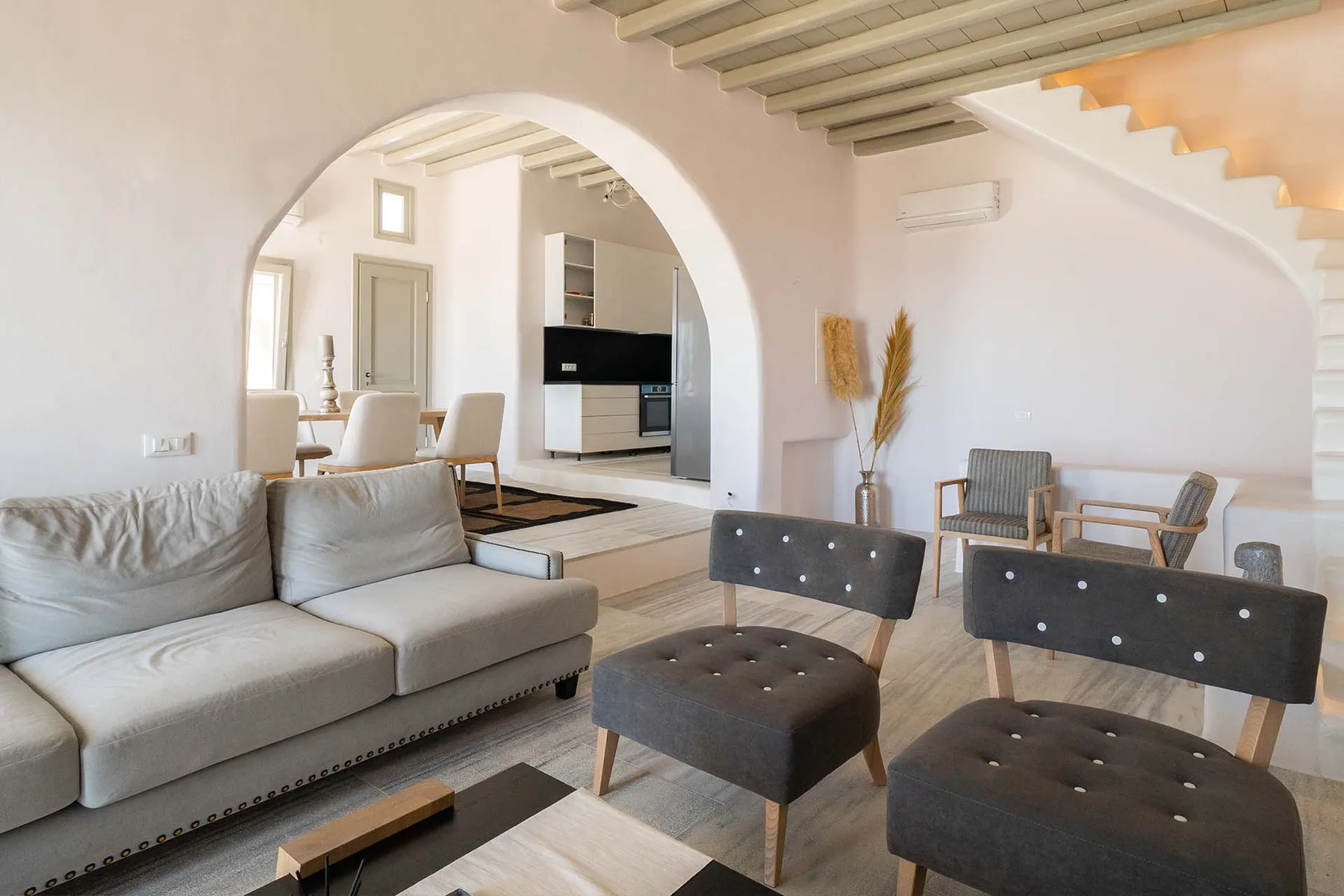 A bright living room with seating, an arched opening, and a staircase.
