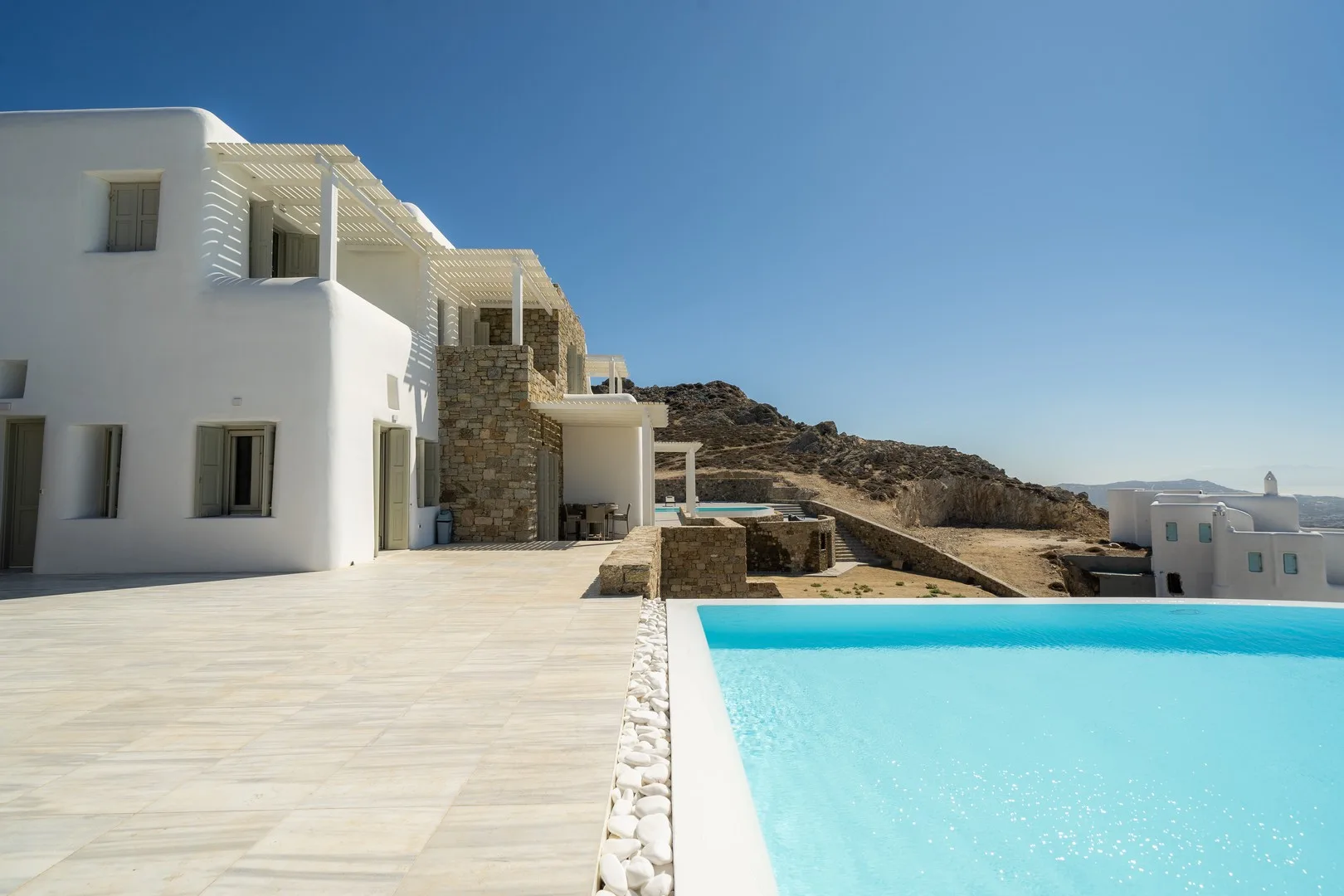 A white villa and turquoise swimming pool sit beside a rocky hillside.