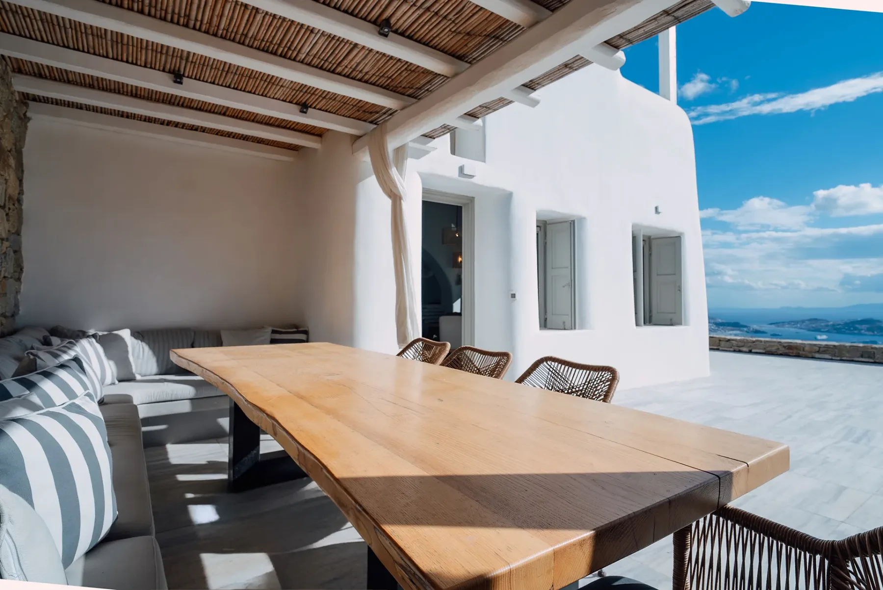 Una zona de comedor exterior cubierta con una mesa larga de madera y asientos acolchados.