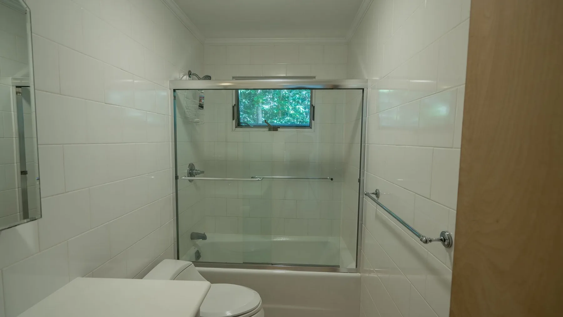 A tiled bathroom with a bathtub and shower behind a glass screen.