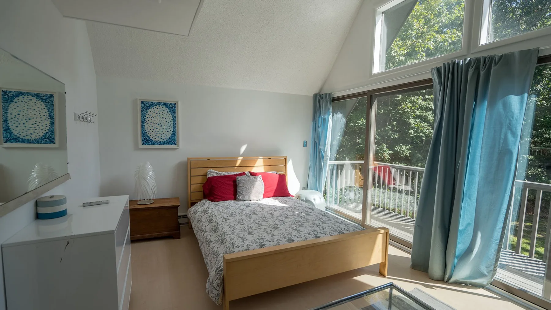 A bright bedroom with a bed beside large windows and blue curtains.