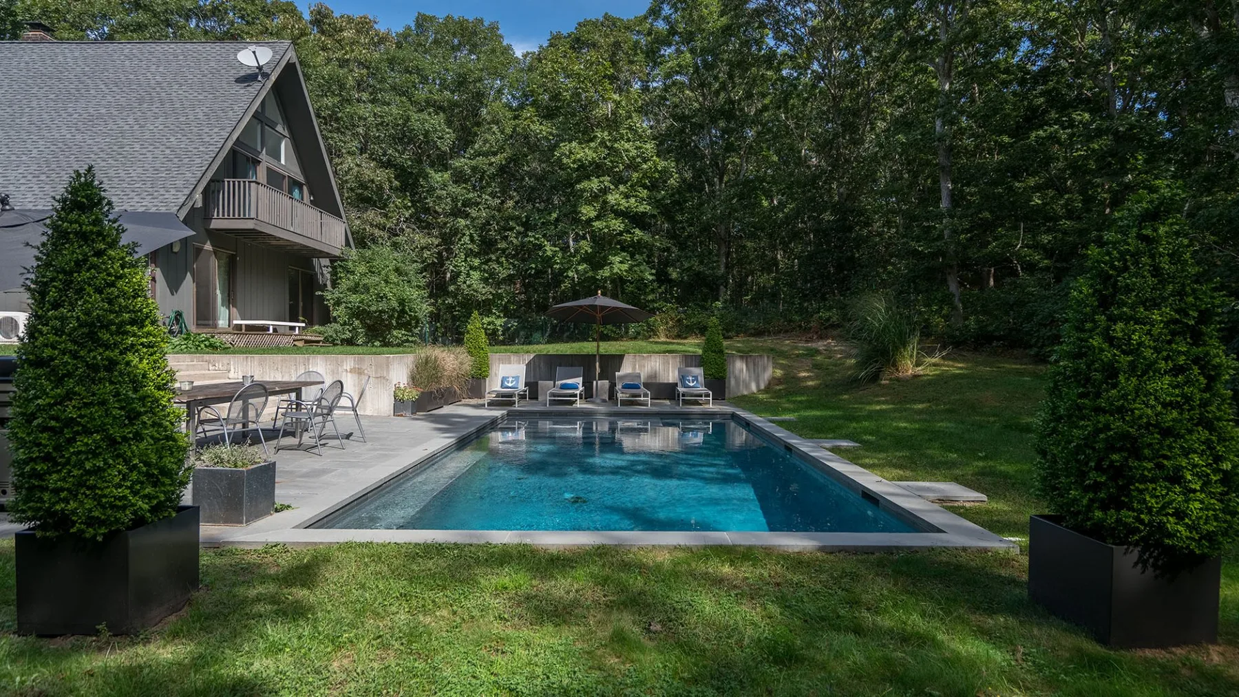 An outdoor swimming pool beside a house, surrounded by greenery.