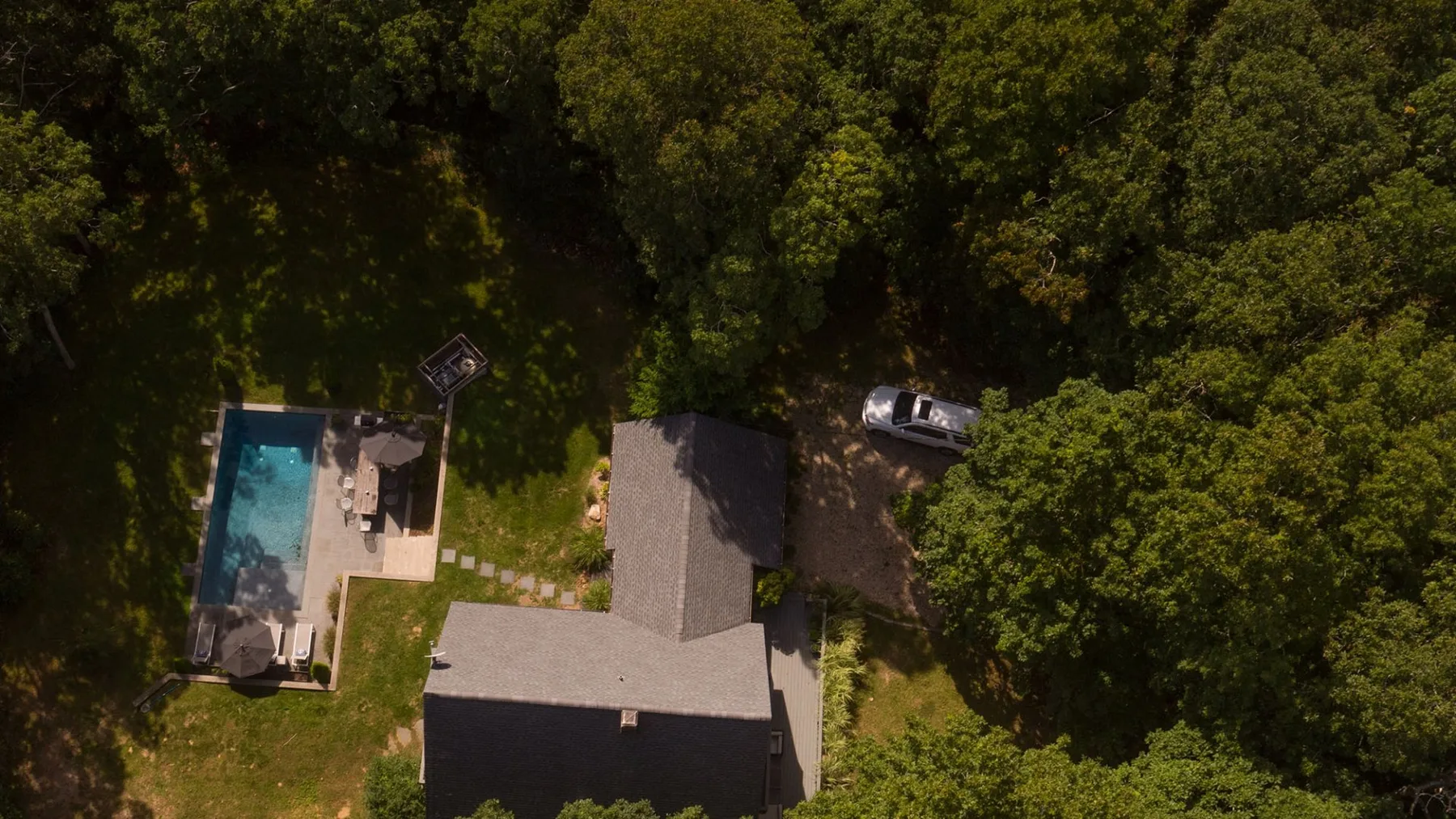 An aerial view shows a house, a swimming pool, and surrounding trees.